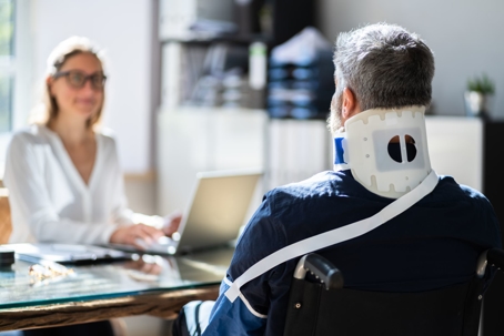 Injured man wearing a neck brace sits at a desk with a lawyer