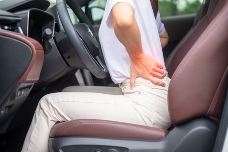 Person sitting in the driver's seat of the car clutching their back in pain