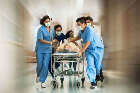 Medical professionals rush a patient on a gurney to a hospital room for treatment