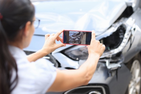 A woman takes a photo of car damage after wreck using her phone.