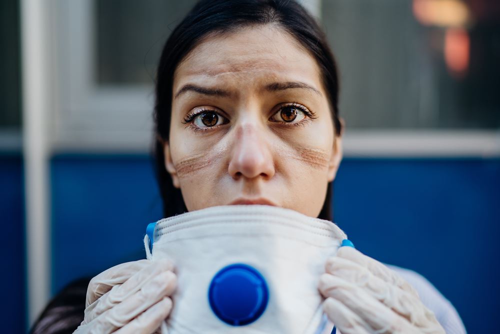 woman with face indentations holding mask after long day of wearing mask